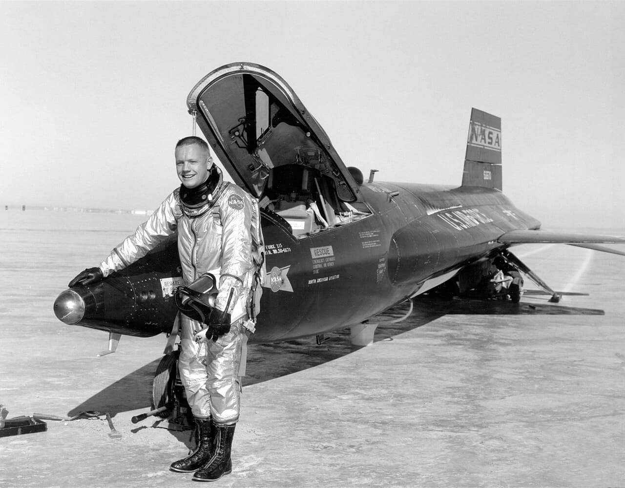 NASA pilot Neil Armstrong beside the X-15 #1 rocket research aircraft on a dry lakebed in silver pressure suit circa 1960